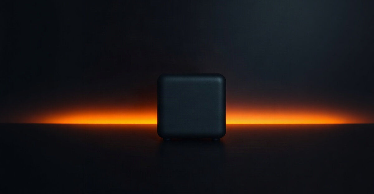 A small black computer cube on a dark desk with amber light behind it